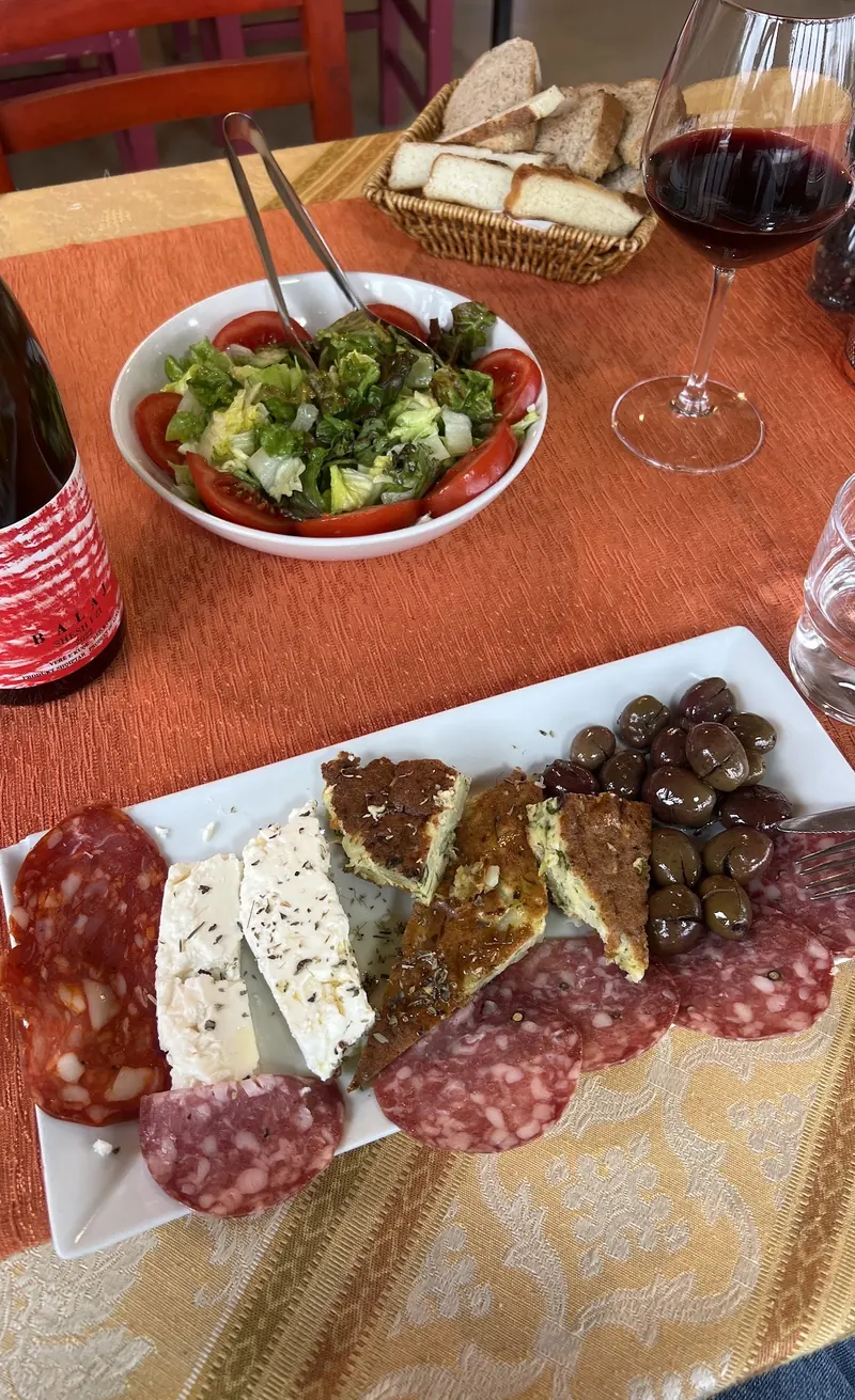 A glass of red wine, cured meats, cheese and olives on an orange tablecloth