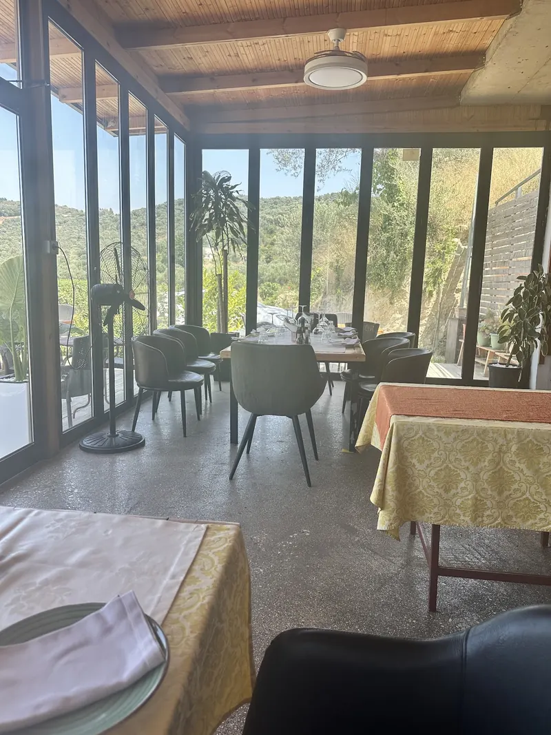 Glass-walled veranda with tables and a view of the wooded hills